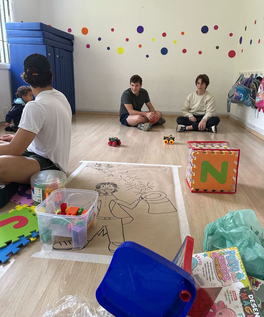 Three members sitting on the floor of a daycare room with toys and a drawing mat